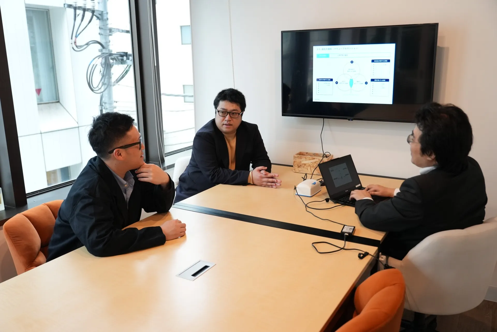 ノートPCのあるテーブルを囲み、3人が打合せをする様子